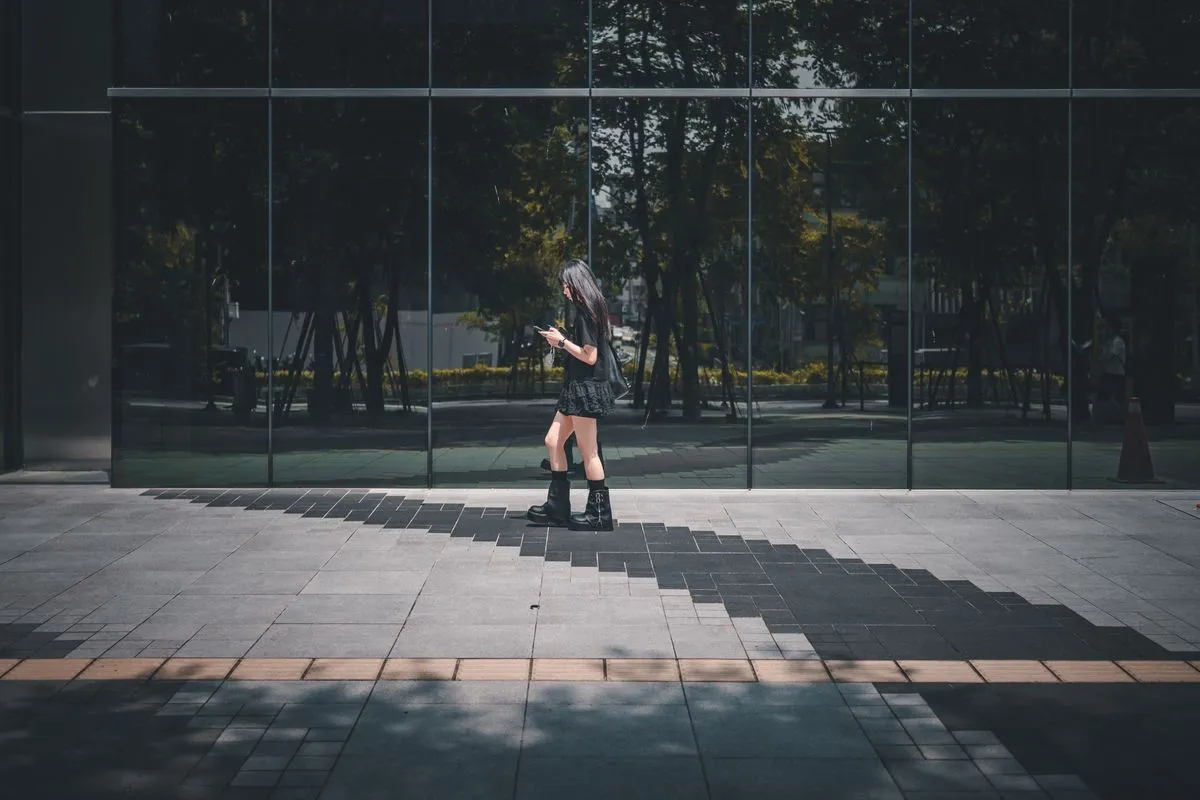 Woman walking alone past a glass office facade, reading her phone