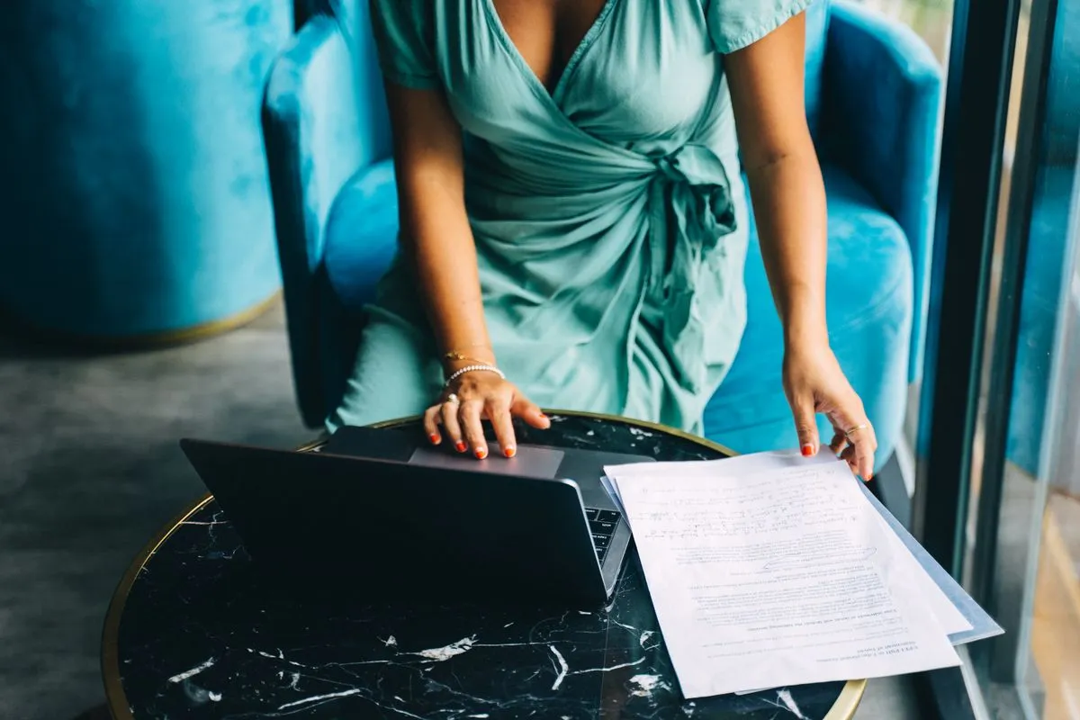 Woman at a marble table holding annotated printed pages beside an open laptop