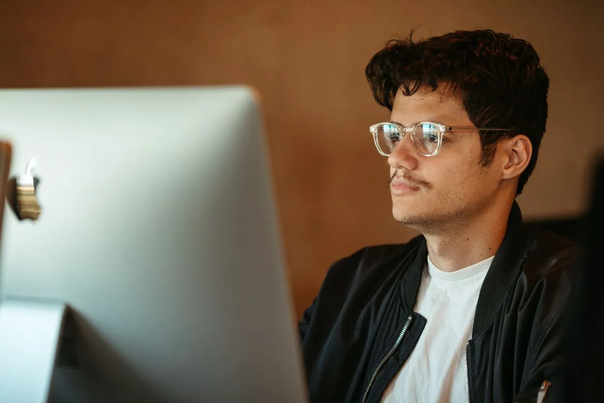 Man in glasses studying a desktop monitor screen at his desk