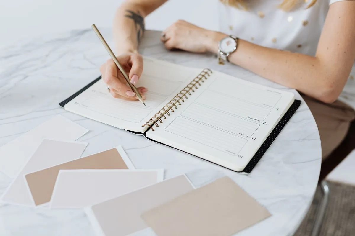 Hand writing in a blank weekly planner on a marble tabletop