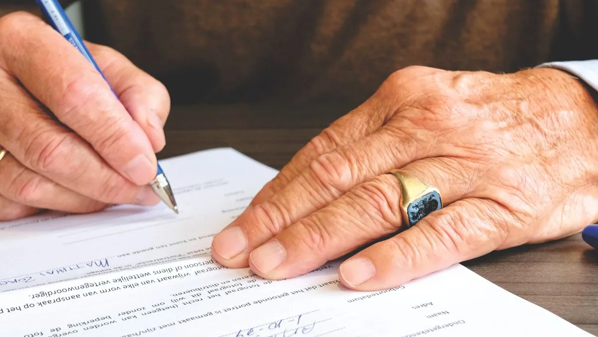 Weathered hands signing the line on a printed form with a pen