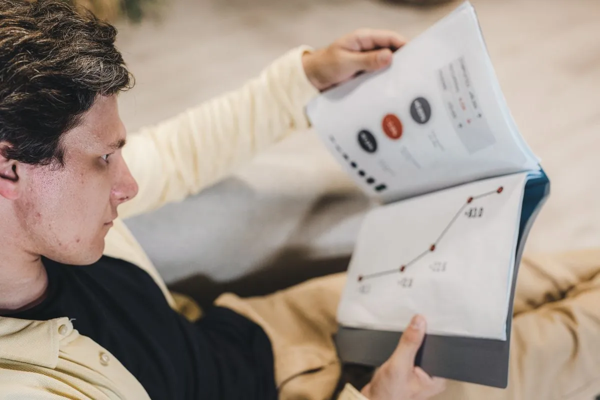 Man turning pages of a printed report showing a rising line chart