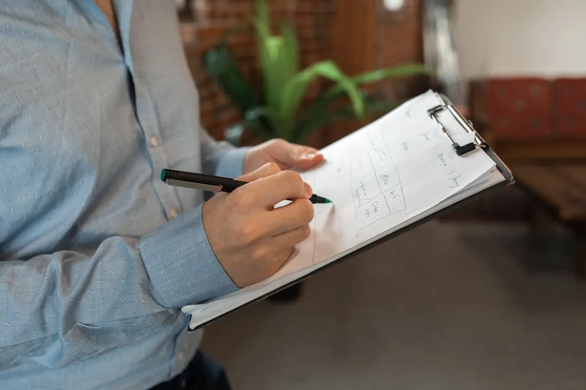 Person in a blue shirt writing with a pen on a clipboard page