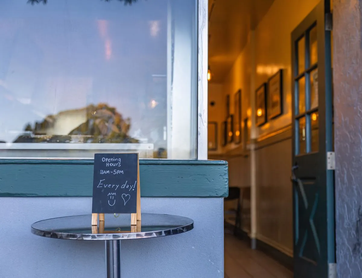 Chalkboard A-frame reading Opening Hours 11AM to 5PM outside a lit doorway