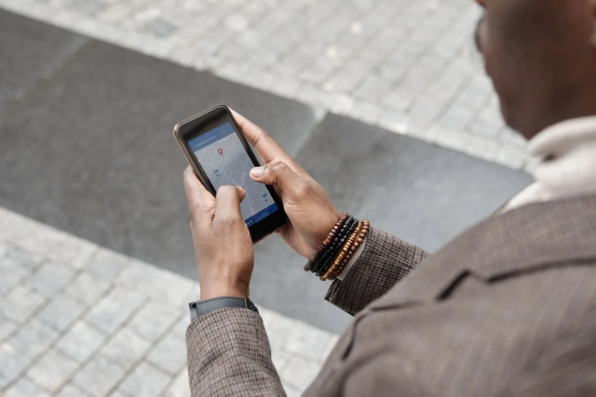 Man on a paved street tapping a map with a pin on his phone