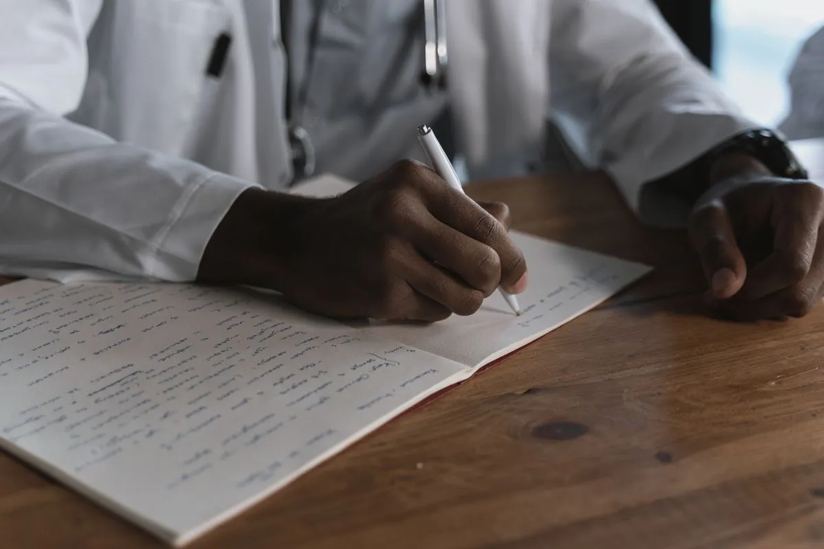 Hand writing in a notebook of dense handwritten notes at a wooden desk